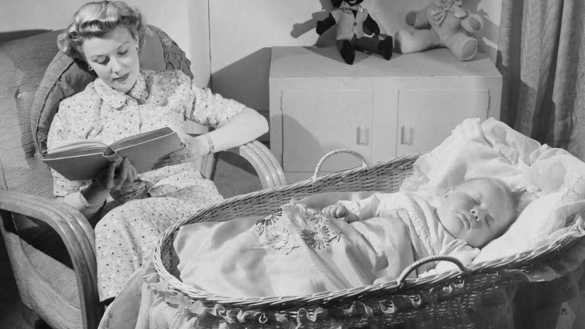 black and white photo of woman reading while her baby sleeps