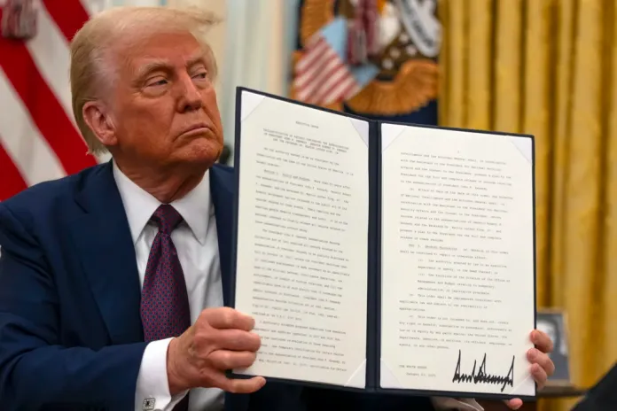 President Donald Trump holds up a signed executive order in the Oval Office of the White House, Thursday, Jan. 23, 2025, in Washington. (AP Photo/Ben Curtis)