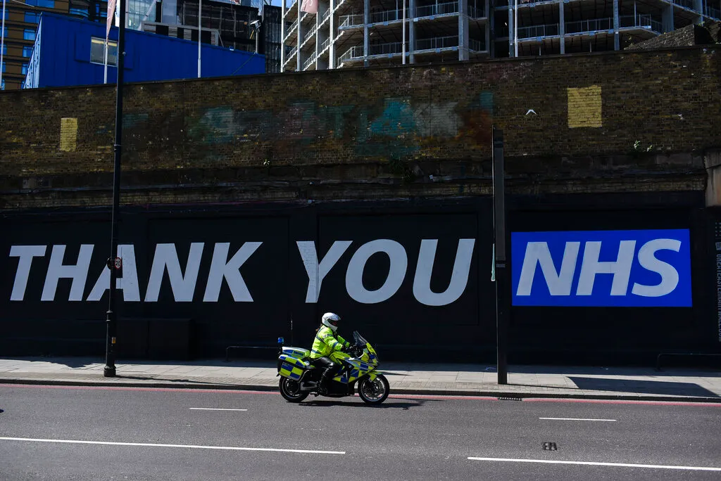 A Police Officer rides past a mural with a message saying 'Thank you NHS' (National Health Service), in London, Tuesday, May 12, 2020. (AP Photo/Alberto Pezzali)