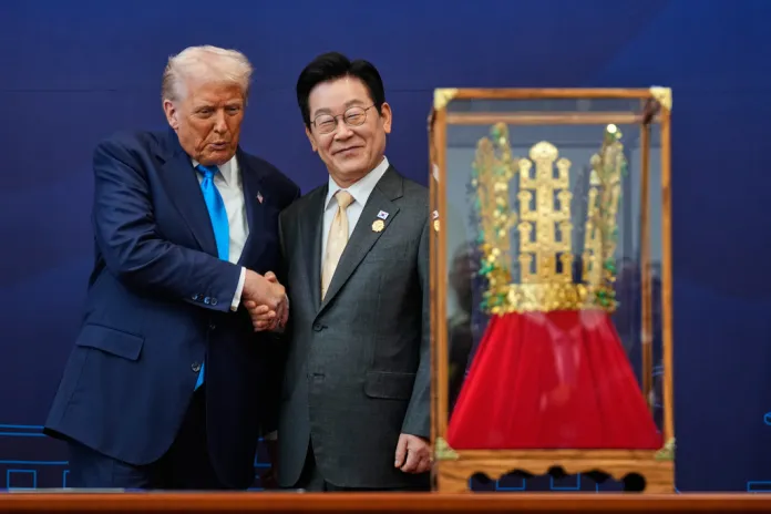 Donald Trump shakes hands with Korean President Lee Jae Myung in front his gold crown gift.
