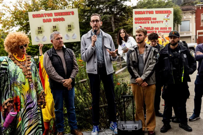 State Sen. Scott Wiener, center, speaks during an annual pumpkin carving event at Noe Valley Park as a group of protesters hold signs.
