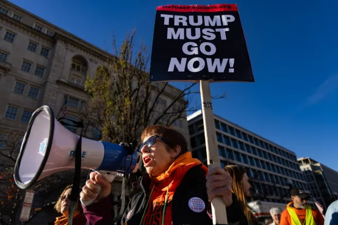 A protester holding a sign that reads "Trump must go now!"