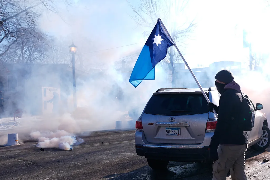 A person holds a Minnesota state flag as federal immigration officers deploy tear gas Saturday, Jan. 24, 2026, in Minneapolis. 