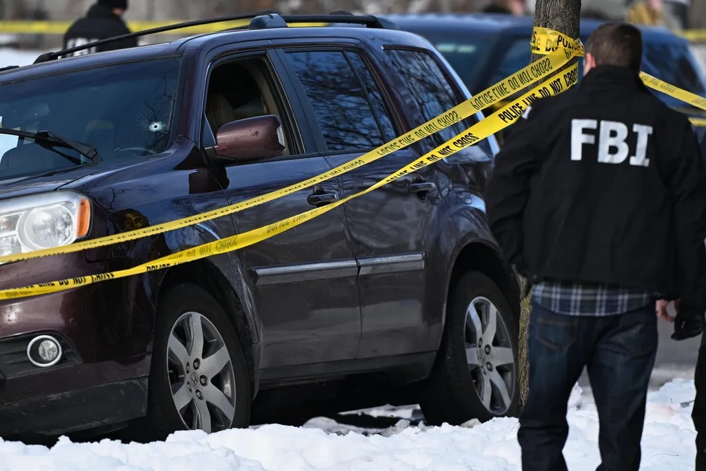 A bullet hole is seen in the windshield of a car as law enforcement officers work the scene of a shooting.
