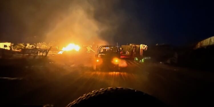 vehicle drives past fiery war scene at night