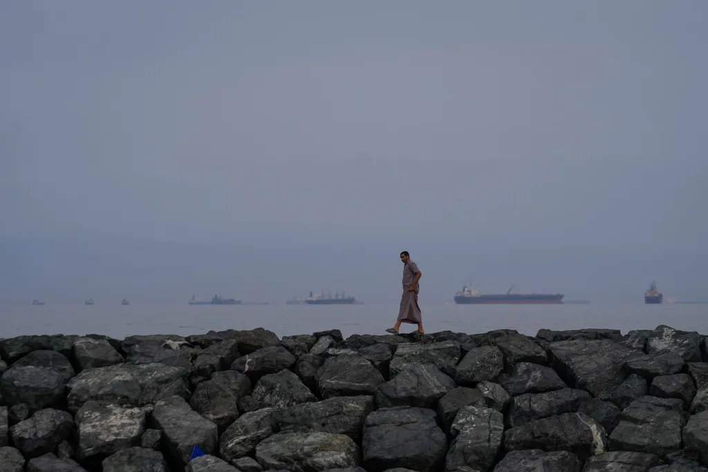 FILE - A man walks along the shore as oil tankers and cargo ships line up in the Strait of Hormuz, as seen from Khor Fakkan, United Arab Emirates, Wednesday, March 11, 2026. 