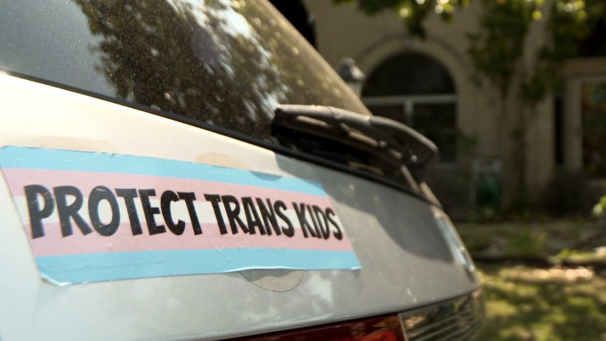 A brightly colored bumpersticker on the back of a white minivan says "protect trans kids."